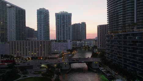 aerial ascending footage of high rise buildings in modern urban borough at twilight. cars driving on bridge over river. miami, usa