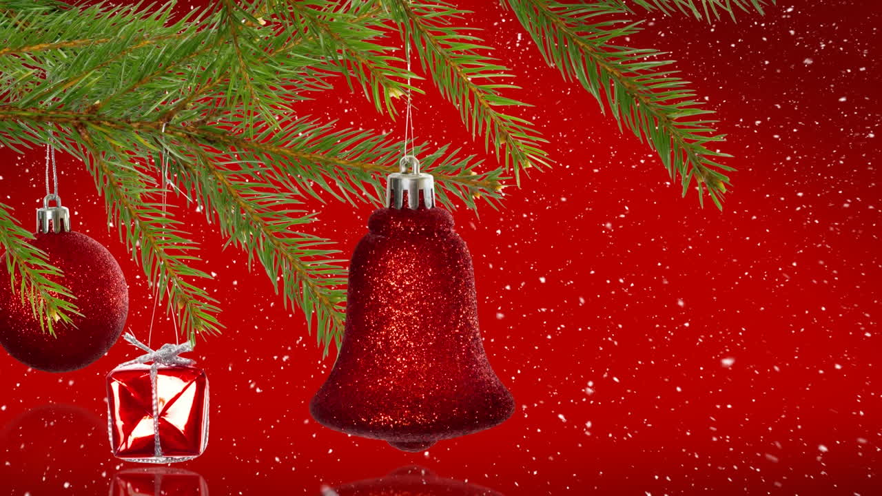 nieve cayendo sobre las decoraciones de navidad colgando sobre la rama del árbol contra un fondo rojo