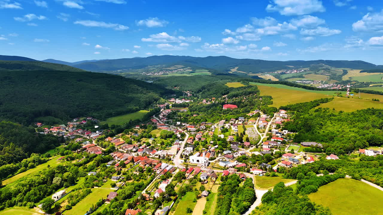 Mountain village scenery. Aerial perspective of a village surrounded by lush green hills under a clear blue sky during a sunny day
