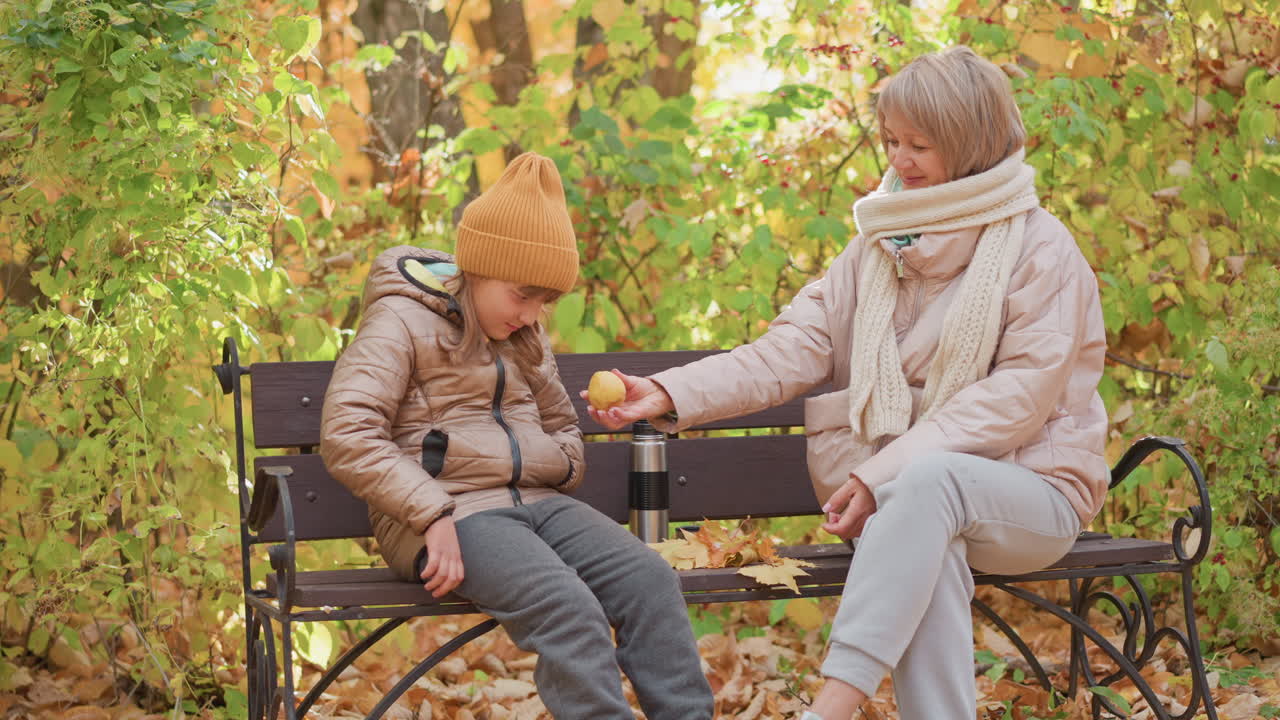 mother and sad daughter sit on bench in forest park surrounded by golden leaves, mother preparing to comfort child with fruit, autumn warmth and emotional moment between parent and child