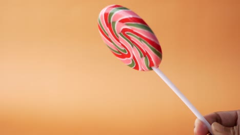 close up of holding lollipop candy against orange background