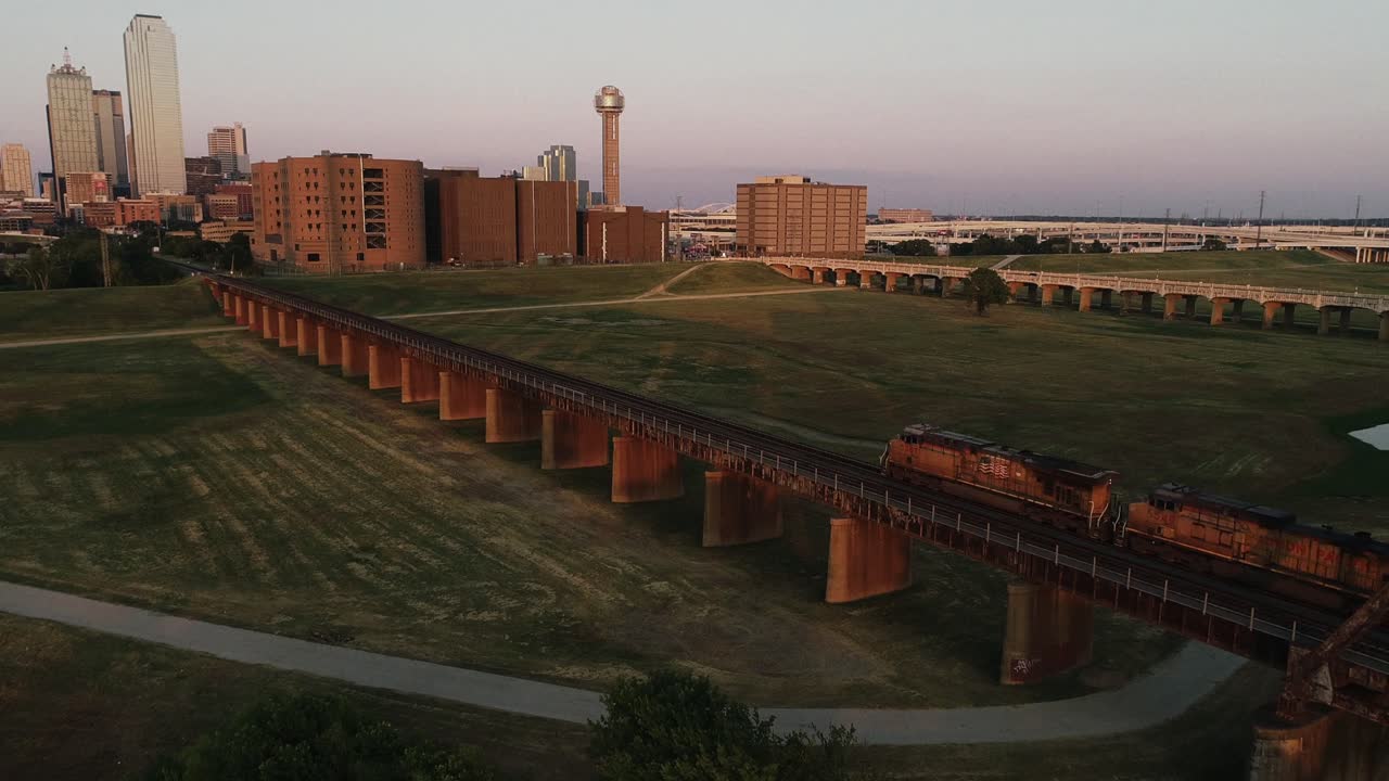 Treno merci diretto nel centro di Dallas, Texas, al tramonto, con la Reunion Tower e lo skyline della città sullo sfondo