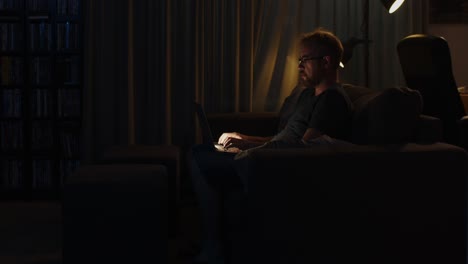 medium view of a man working on his laptop late at night on his living room couch