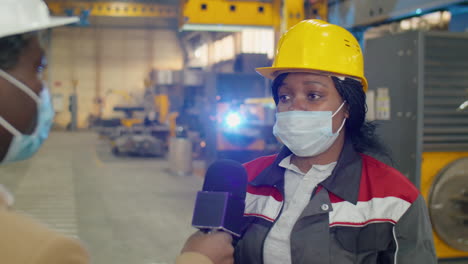 female factory worker in mask giving interview to reporter