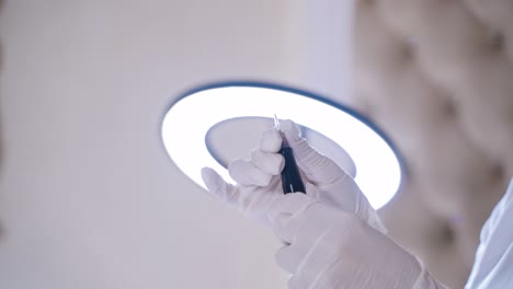 a permanent makeup master checks his professional instrument before performing the procedure in the room on the background of lamp. close-up. blurred background.