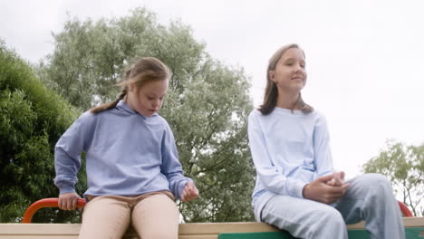 Little-girl-with-down-syndrome-talking-with-her-blonde-friend-in-the-park.-Then-other-boy-approachs-and-greets-them