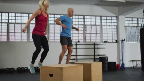 fit caucasian woman and man jumping on pylo boxes at the gym