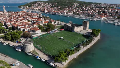 aerial establishing fly trogir, unesco heritage croatian town, historic buildings next to soccer field