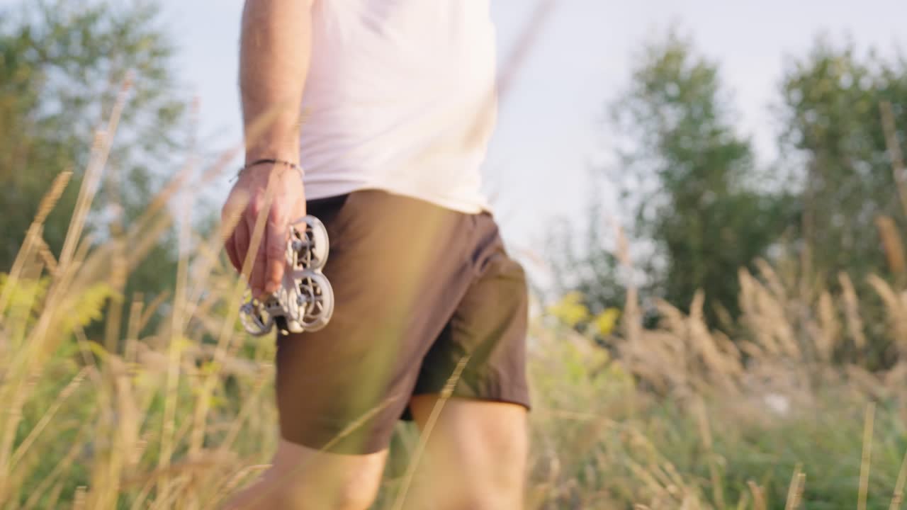 Person walk in long dry grass meadow and hold compact drone in hands, Czechia
