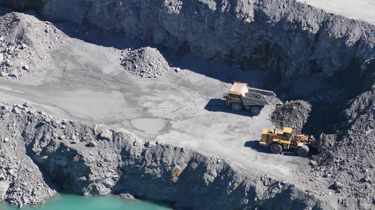 Drone footage captures excavators and trucks working in a sunlit quarry, highlighting industrial activity and rugged terrain