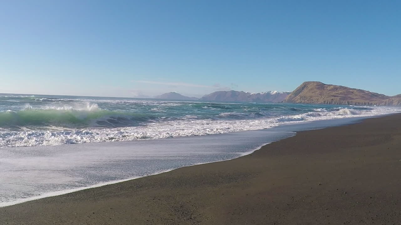 un hermoso día soleado con un cielo azul claro a lo largo de una playa de arena con montañas a lo lejos en la isla de kodiak, alaska