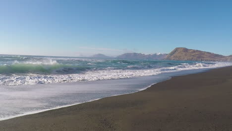 Un-Hermoso-Día-Soleado-Con-Un-Cielo-Azul-Claro-A-Lo-Largo-De-Una-Playa-De-Arena-Con-Montañas-A-Lo-Lejos-En-La-Isla-De-Kodiak,-Alaska