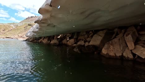 glacial meltwater pool with overhanging snow and rocky alpine terrain in alpe veglia natural park, piedmont, italy