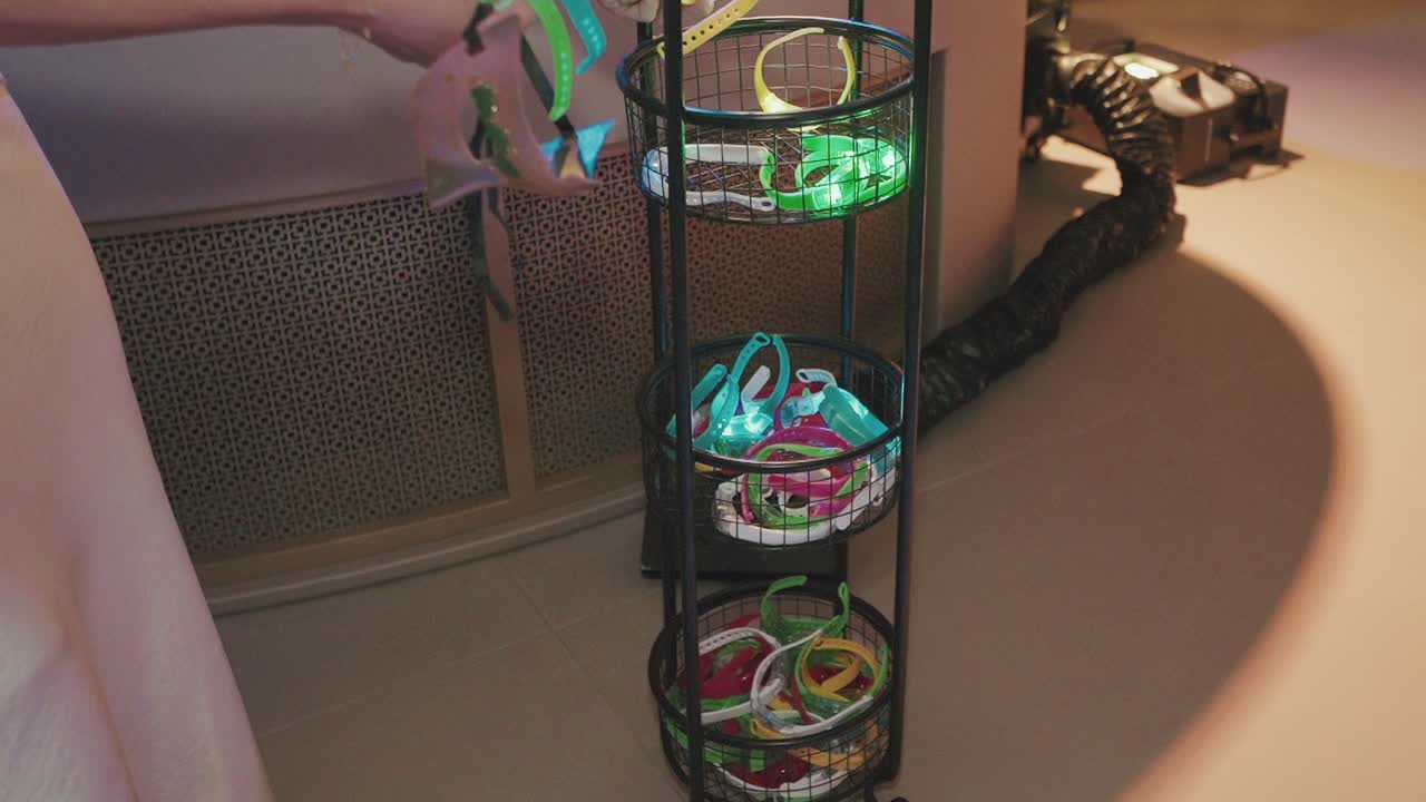 Manos eligiendo pulseras de neón y máscaras de un puesto con cesta