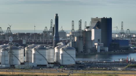 vista aérea de la torre de la central eléctrica de carbón con tanques de almacenamiento de petróleo y turbinas eólicas giratorias durante el día soleado - puerto de rotterdam, países bajos