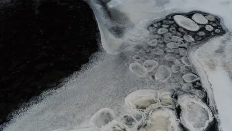 piezas de hielo congeladas en patrón flotan en la superficie del agua del estanque oscuro cerca de la capa de hielo