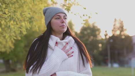 mujer cansada con suéter y gorra con dificultad para respirar en el parque por la mañana