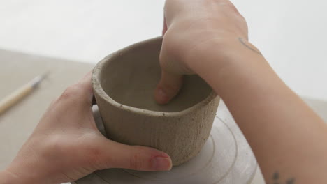 skillfully molding a clay cup's surface with fingers, creating intricate texture in a charming studio