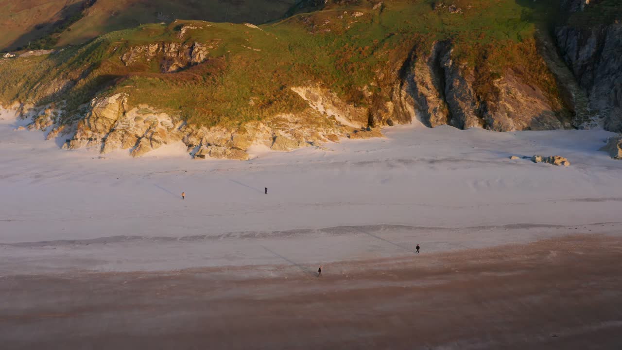 Stationary Aerial View of Four People Walking Across Maghera Beach With Rugged Mountain Background During a Golden Hour