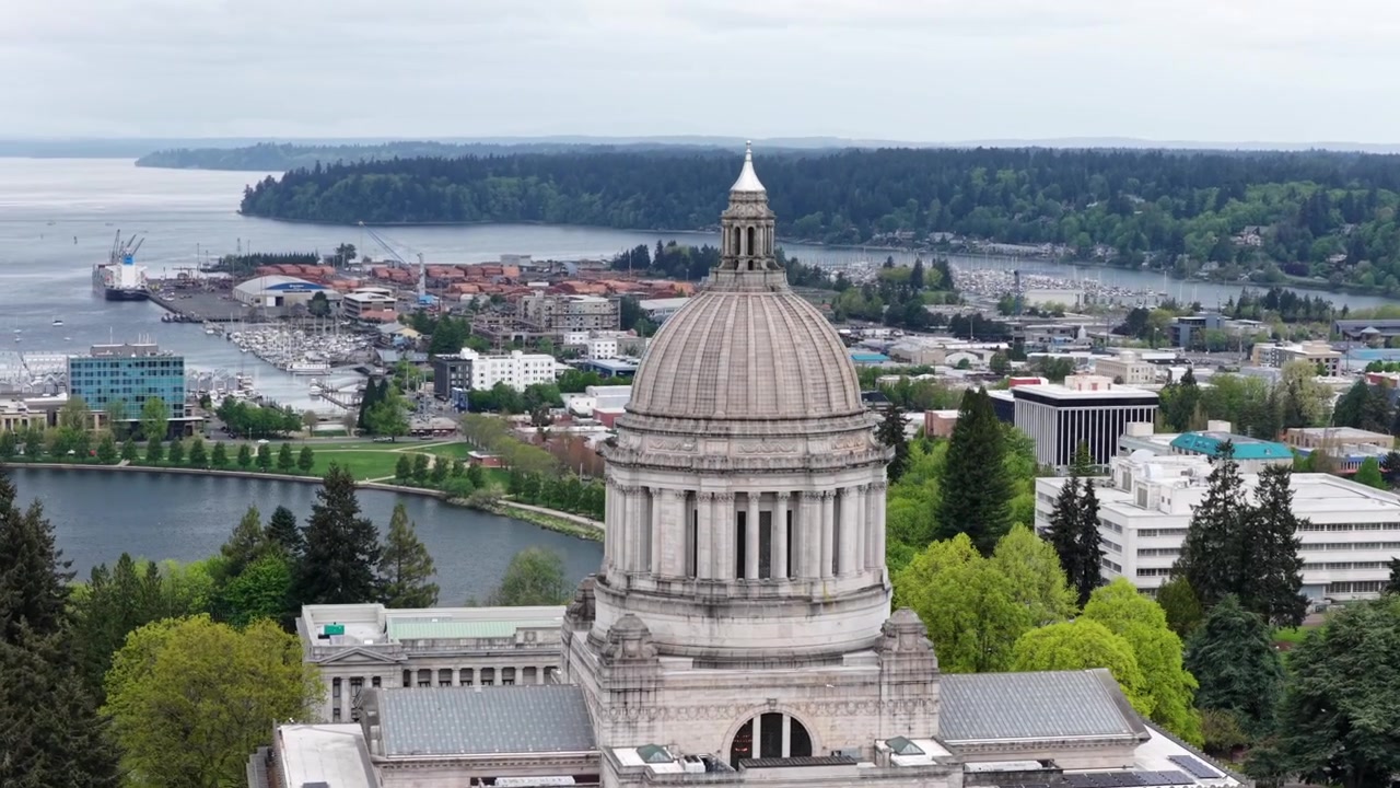 Orbita aerea con drone dell'edificio del Campidoglio dello Stato di Washington a Olympia, Washington, con la cupola iconica, il paesaggio urbano circostante e il lungolago del Lago Capitol nel Pacifico nord-occidentale, USA. Ampia inquadratura.