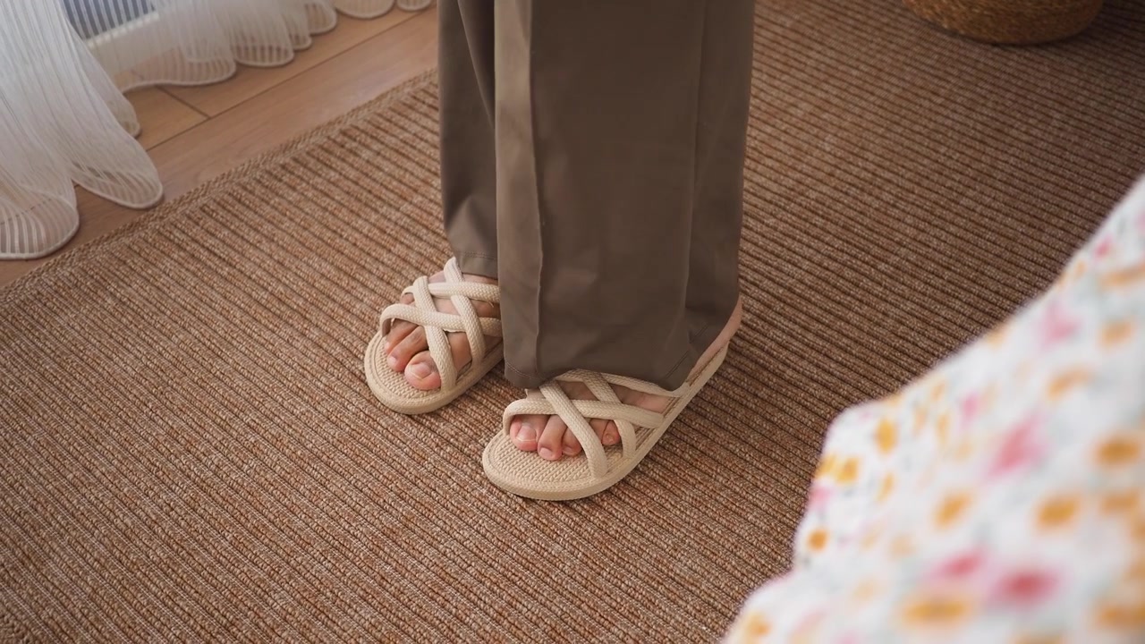 Person tar på seg beige sandaler på et brunt teppe