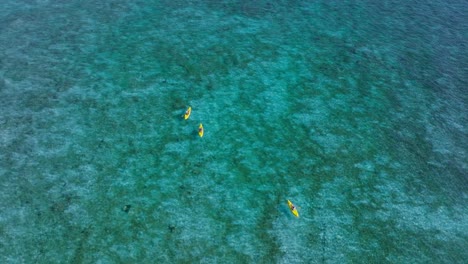 Agua-De-Mar-Azul-Turquesa-Perfecta-Con-Tres-Personas-En-Kayaks-Amarillos,-Actividad-De-Verano,-Antena