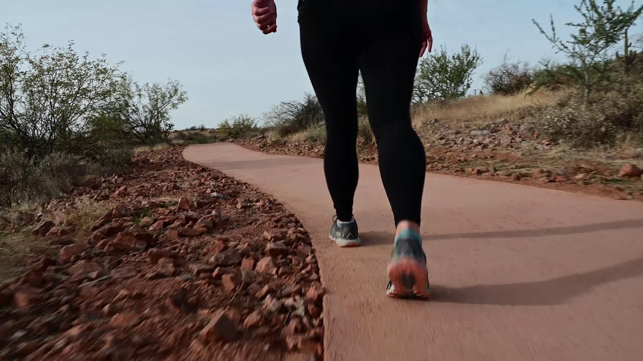 mujer de ángulo bajo caminando por un sendero pavimentado del desierto