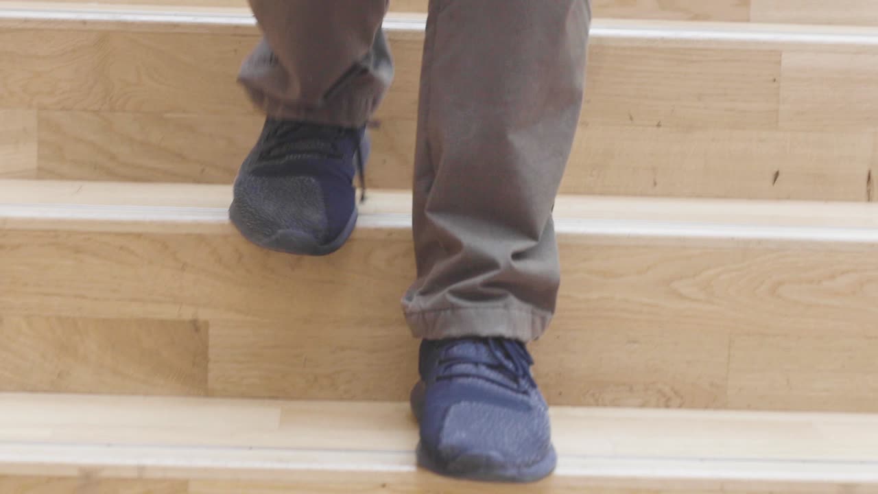 крупный план мужчины, идущего по широкой деревянной современной лестнице в темных туфлях и джинсах