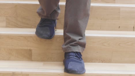 primer plano de un hombre caminando por una amplia escalera moderna de madera con zapatos oscuros y jeans en