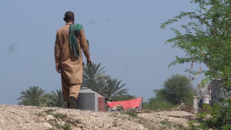 Toma-En-ángulo-Bajo-De-Un-Local-Que-Pasa-Caminando-Por-Un-Campamento-Improvisado-Al-Borde-De-La-Carretera-Hecho-Después-De-Las-Inundaciones-En-Sindh,-Pakistán-Durante-El-Día