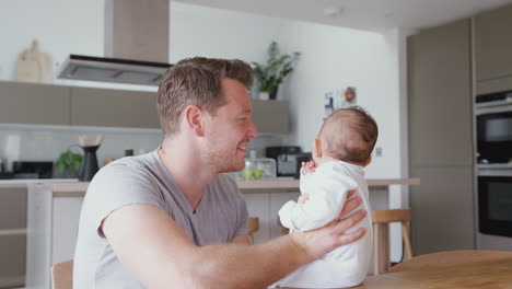 padre amoroso sosteniendo a su hija de 3 meses en la cocina en casa jugando un juego