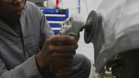 mecánico de automóviles afroamericano usando un molinillo de ángulo en el costado de un automóvil