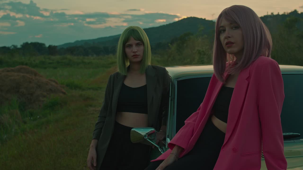 Two Stylish Women Posing by a Vintage Car at Sunset