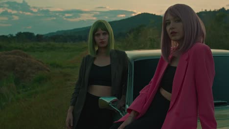 two stylish women posing by a vintage car at sunset