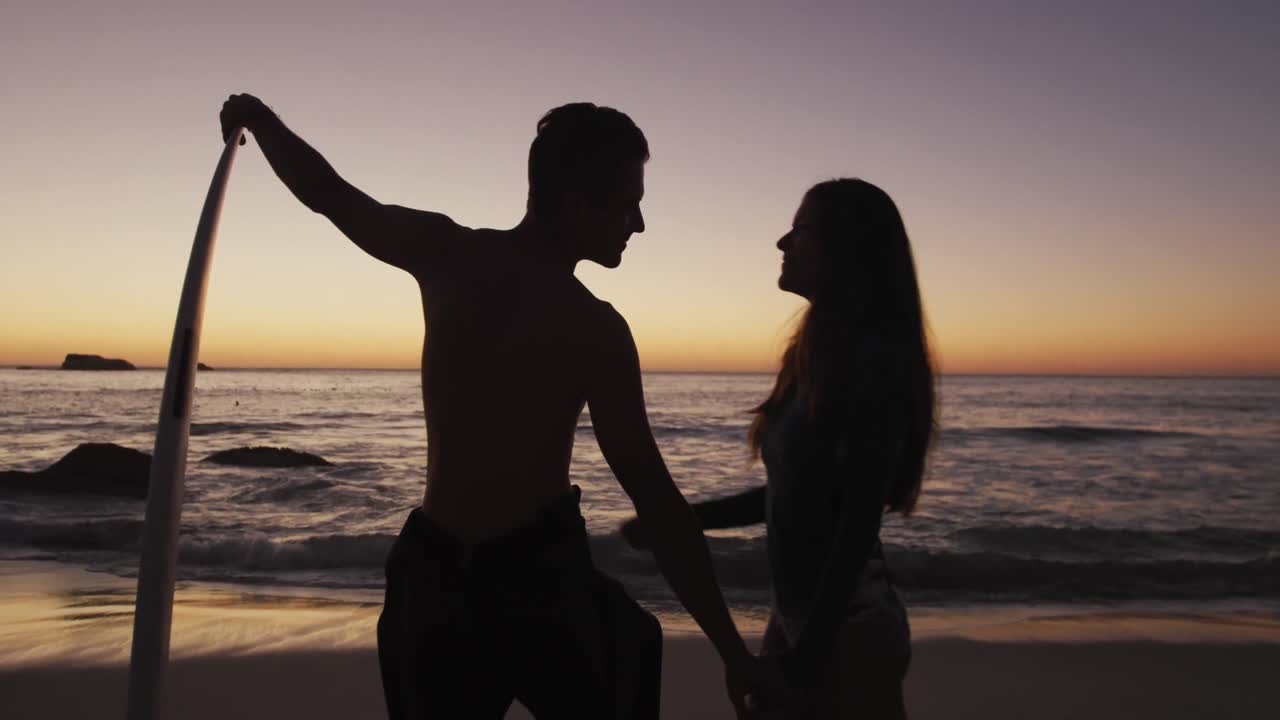 젊은 성인 부부가 해가 지는 해변에서 휴식을 취하고 있습니다.