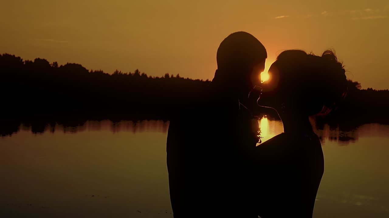 강 에서 해가 지는 배경에 안고 있는 두 젊은이 1개의 느린 동작