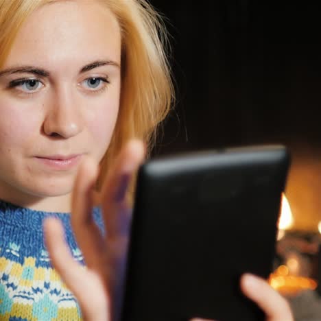 a young woman uses tablet near a christmas tree on a background of fire 1