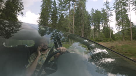 Hombre-Hablando-Por-Teléfono-Mientras-Conduce-Por-Un-Camino-Forestal-De-Montaña