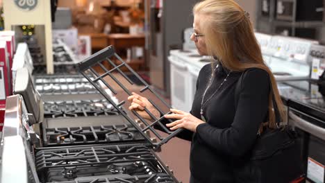 Mujer-Rubia-Bastante-Madura-Mirando-Las-Características-Y-Beneficios-De-Una-Estufa-De-Gas-En-Una-Tienda-De-Electrodomésticos-De-Cocina