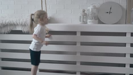 little girl with ponytail jumps on wooden brown floor