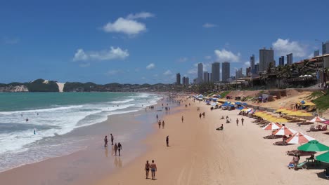 Tiefflug-über-Menschen-Am-Sandstrand-Und-Skyline-Von-Ponta-Preta