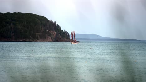 View-of-sailboat-through-foreground-reeds-and-grass-that-are-out-of-focus,-slow-motion