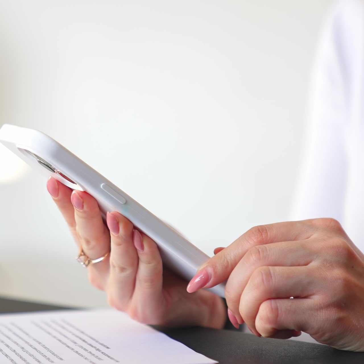 Female manicured hands hold the telephone. Lady presses some buttons on white phone at white backdrop. Close up