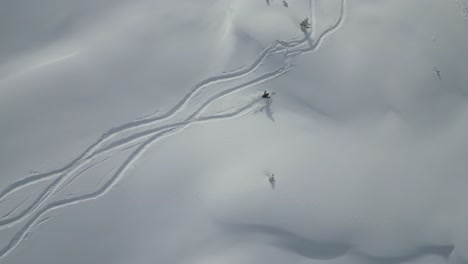 aerial following young sports man skiing down snow covered glacier mountain range slope in snowy alpine scenery, top down view