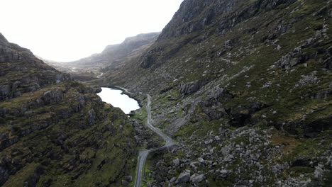 Cinematic-drone-shot-passing-through-the-Gap-of-Dunloe,-revealing-a-small-pond-beyond-the-rocky-cliffs