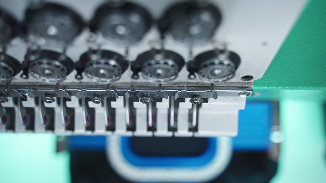 Spools of thread in an embroidery machine ready for stitching, high overview of bobbin spinning and needle action pulsing
