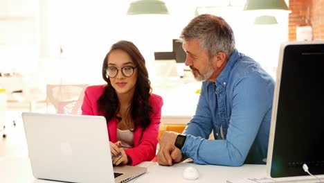 Male-and-female-executives-discussing-over-laptop-at-desk