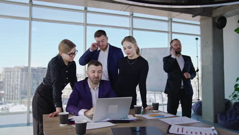 teamwork and brainstorming at office meeting. colleagues gathered around their chief and look at his laptop. male manager speaks on the phone at backdrop.