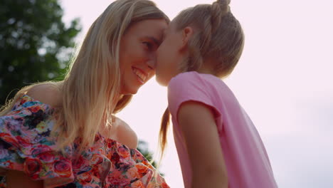 daughter kissing mother in city park. woman and girl enjoying sunset outdoor.