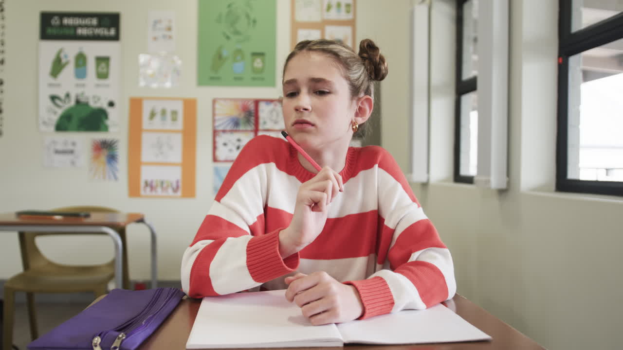 In classe, giovane ragazza che pensa mentre è seduta al banco con un quaderno aperto, a scuola.